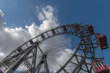 A huge Victorian Metal Ferris Wheel in a large public park in Vienna, Austria with a blue sky and white fluffy clouds above.