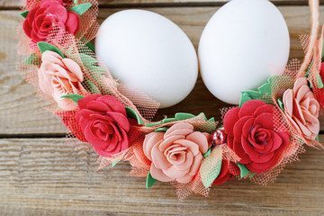 White chicken eggs in a flower wreath on a wooden table
