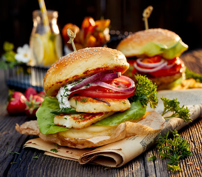 Vegetarian burger with grilled halloumi cheese, fresh lettuce, tomato, cucumber and onion with the addition of yoghurt mint sauce on a wooden rustic table