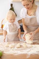 Little girl and her blonde mom in beige aprons  playing and laughing while kneading the dough in the kitchen. Homemade pastry for bread, pizza or bake cookies