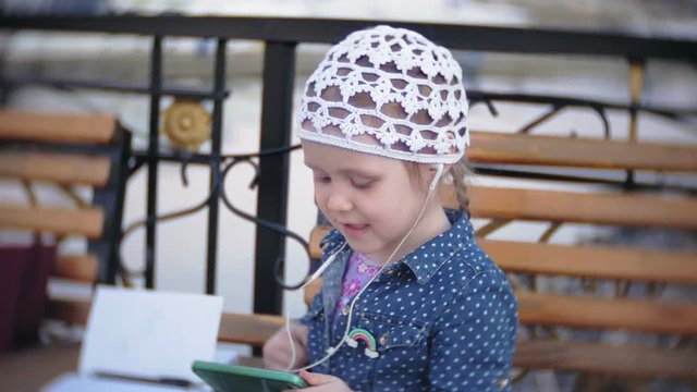 Little stylish beautiful gerl, on city streets listening to music in l headphones.