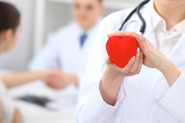 Female doctor holding heart in her hands.  Doctor and patient sitting in the background. Cardiology in medicine and health care