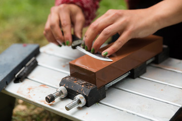 Woman sharpens a knife on a wet block outdoors