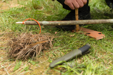 Man using knife and dry materials with friction bow to start a fire in the forest
