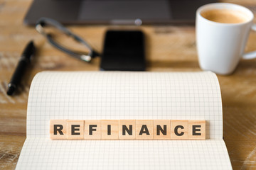 Closeup on notebook over wood table background, focus on wooden blocks with letters making Refinance text