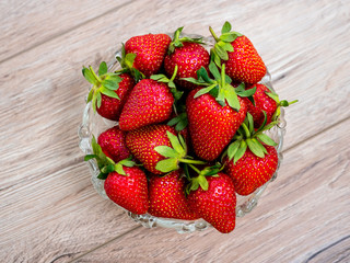 Heap of fresh strawberries in glass bowl on rustic white wooden background