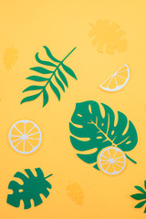 Fototapeta na wymiar Tropical leaves pattern. Green monstera and fern leaves with orange and lemon slices on a bright yellow background. Summer vacation concept with paper craft fruits