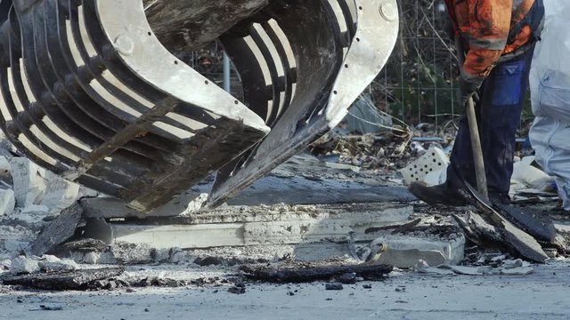 Demolition Worker Shoveling And A Hydraulic Excavator Grapple Or Gripper Picking Up And Sorting Torn Down Building Materials In Front Of Him.