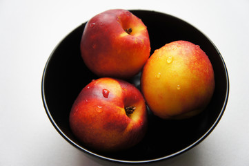Three yellow and red nectarine fruits in black bowl 