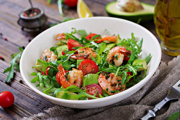 Fresh salad bowl with shrimp, tomato, avocado and arugula on wooden background close up. Healthy food. Clean eating.