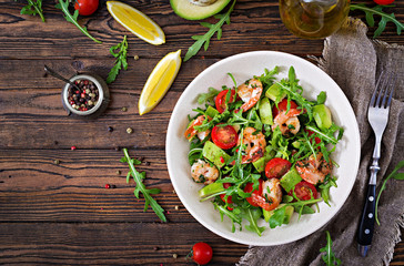 Fresh salad bowl with shrimp, tomato, avocado and arugula on wooden background close up. Healthy food. Clean eating. Top view. Flat lay. - Powered by Adobe