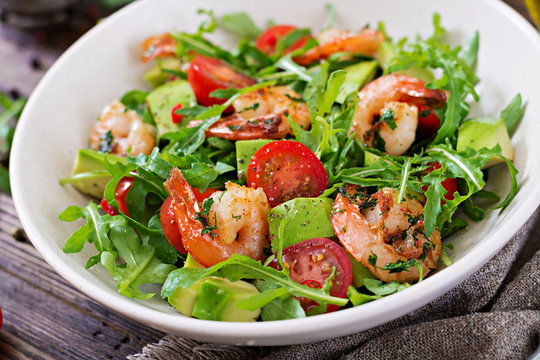 Fresh salad bowl with shrimp, tomato, avocado and arugula on wooden background close up. Healthy food. Clean eating.