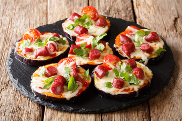 light snack from hot eggplants with cheese, tomatoes, sausages and sauce close-up on the table. horizontal