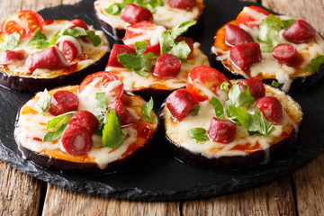 Mini pizza from eggplants with mozzarella, tomatoes, sausages and greens close-up. horizontal