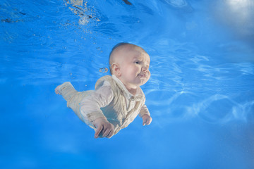Fototapeta na wymiar 3 months boy in dress learning to swim underwater in the pool