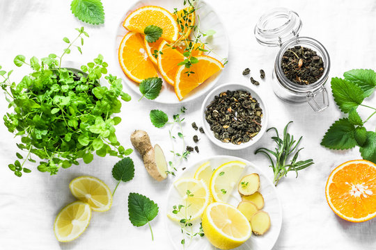 Ingredients for making cold aromatic green tea - dry green tea, lemon, orange, ginger, mint, rosemary on a light background, top view. Flat lay