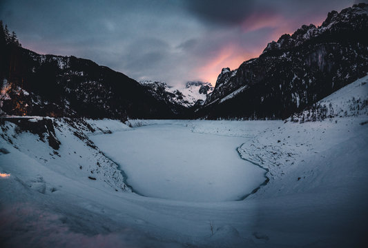 Die Gosauseen zum Salzkammergut gehörender Bergsee im Gosautal in Oberösterreich, Österreich bei Nach mit warmen Lichtern die sich in den Wolken über den Bergen zeigen im Winter bei Nacht