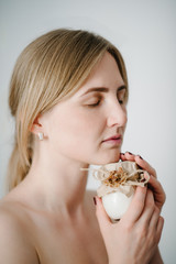 A beautiful young woman with clean fresh skin holds a white jar with a face cream isolated on grey background. The concept of the use of cosmetics for the body and moisture. Facial care.