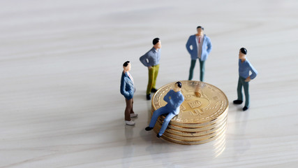 Four&nbsp;miniature&nbsp;men&nbsp;surrounded&nbsp;by&nbsp;pile&nbsp;of&nbsp;bitcoin,&nbsp;and&nbsp;a&nbsp;miniature&nbsp;man&nbsp;sitting&nbsp;on&nbsp;top&nbsp;of&nbsp;a&nbsp;coin.