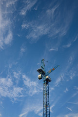 Construction crane isolated against a bright blue sky with scattered white clouds vertical