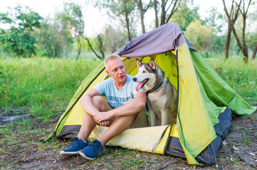 Man with husky dog in tent outdoors. Concept of friendship of the man and dog