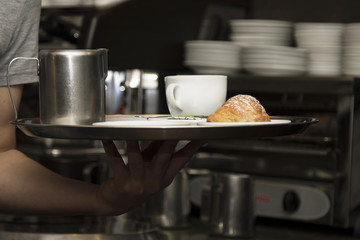 waiter serving coffee and croissant on tray