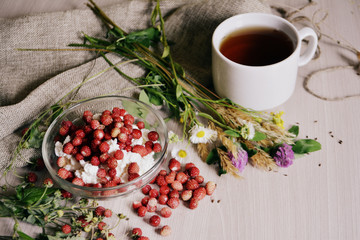 A Cup of tea, cottage cheese with berries, flowers and wild strawberries on the table. Breakfast. Still-life
