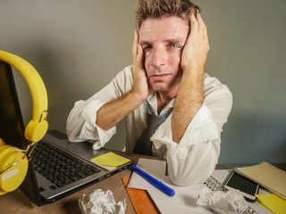 attractive sad and desperate man in lose necktie looking messy and depressed working at laptop...