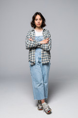 Full length image of brunette woman posing with crossed arms and looking at the camera over gray background