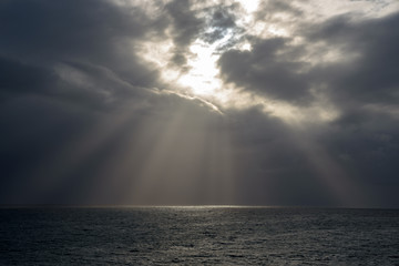 Naklejka na ściany i meble Dark clouds and sun rays on a sea. Sunlight. Madeira Island.