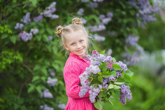 Cute beautiful girl with a bouquet of lilac in the park in the summer