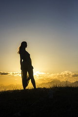 Fototapeta na wymiar silhouete of girl in dress standing on grass in sunset mountains