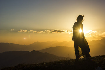 silhouete of girl in dress standing on grass in sunset mountains