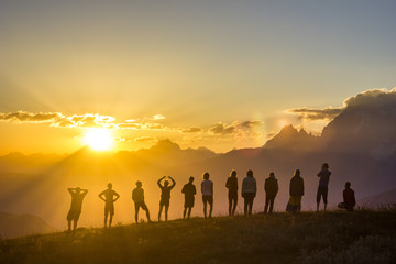 group of people with hands up standing on grass in sunset mountains - Powered by Adobe