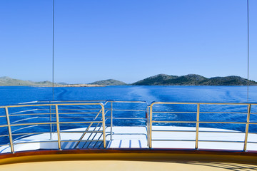 Stern of a sailing boat heading away from islands on a blue sea