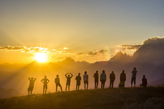 group of people with hands up standing on grass in sunset mountains