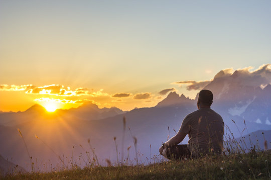 man sitting on grass at sunset in mountains