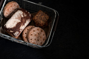 A loaf of bread and wholemeal flour in a metal basket on a black background, top view.