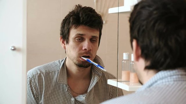 Tortured sleepy only waking man in front of the mirror with a toothbrush in his mouth.