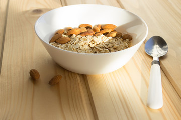 Proper balanced diet: oat flakes and almonds in a white cup on a light wooden table