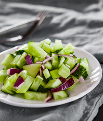 Cucumber and onion salad in a white plate on old wooden table.
