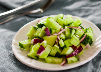 Cucumber and onion salad in a white plate on old wooden table.