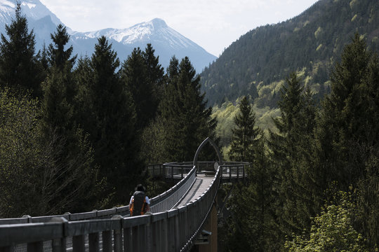 Young adult male walking over a bridge at a tree top walkway in the german alps