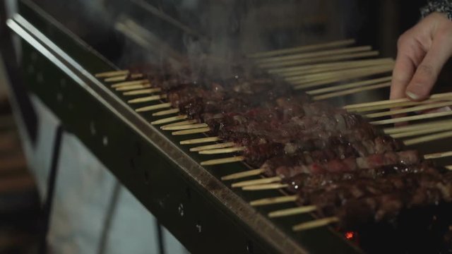 A girl's hand cooking arrosticini on the grate.