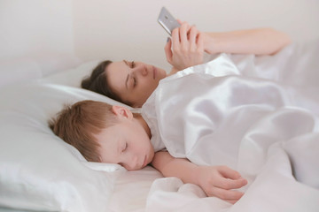 Fototapeta na wymiar Mom woke up and browsing internet in her mobile phone. Her son is still asleep.