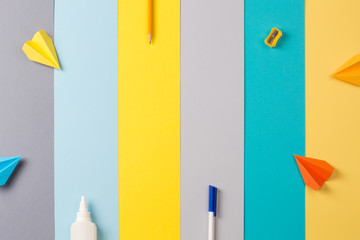school and office supplies on bright striped background. minimum set in yellow, blue, grey and orange color: pen, pencil, sharpener, glue. concept: back to school, minimalism. Flat lay, copy space