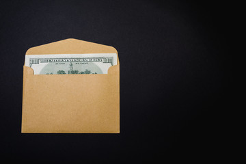One hundred dollars in a brown envelope on a black background