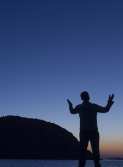 Silhouetted man raises his arms towards the sky at sun rise