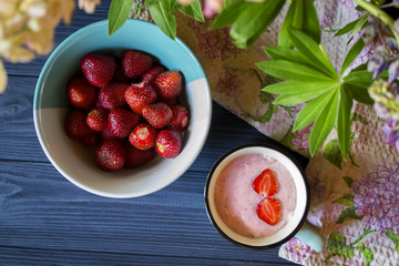 Strawberry dessert. A mug with strawberry creamy fresh and bowl with ripe strawberries on a dark blue wooden table. Beautiful food still life.	