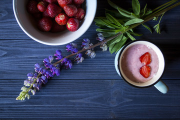 Strawberry dessert. A mug with strawberry creamy fresh, bowl with ripe strawberries and lupine on a dark blue wooden table. Beautiful food still life.	